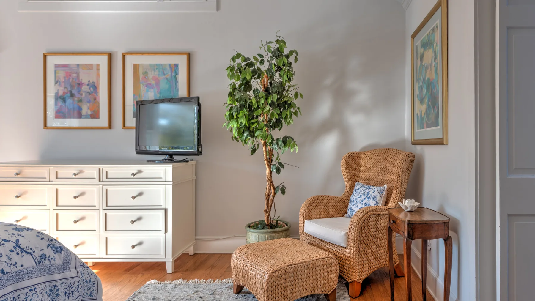 A bedroom sitting area with a wicker chair, matching ottoman, and television.