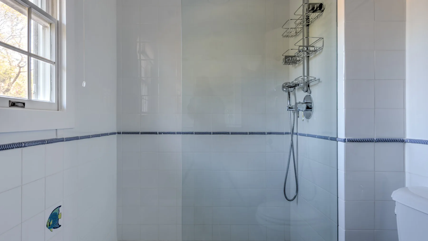 A tiled bathroom with a wall-mounted shower and a window.