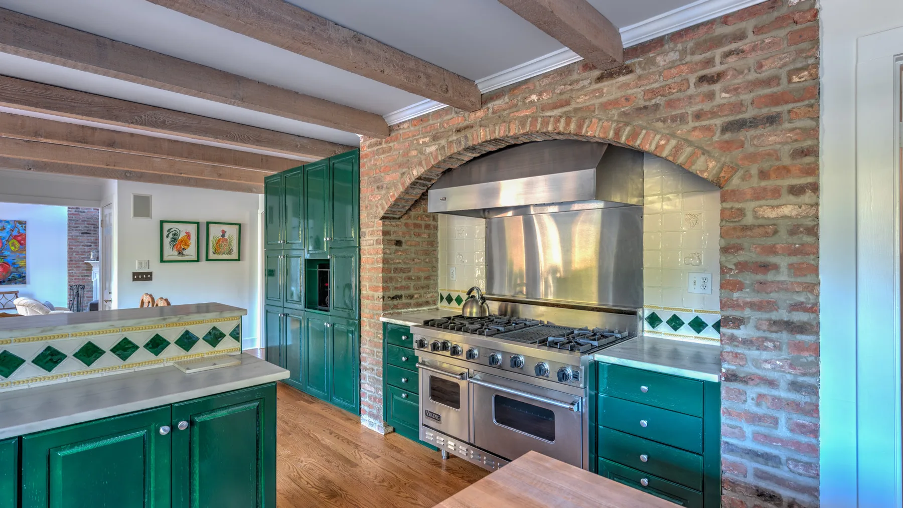 A kitchen with green cabinetry, a stainless steel range, and exposed brick.