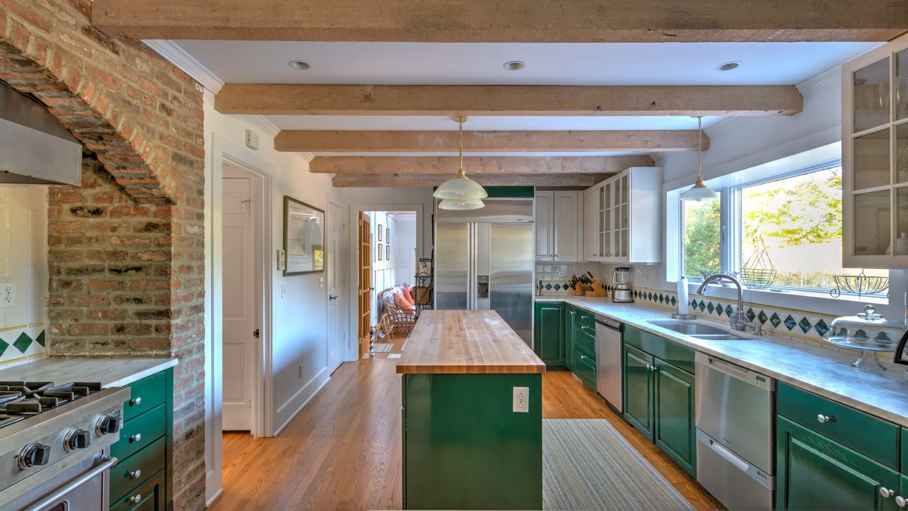 A bright kitchen with green cabinetry, a central island, and large windows.