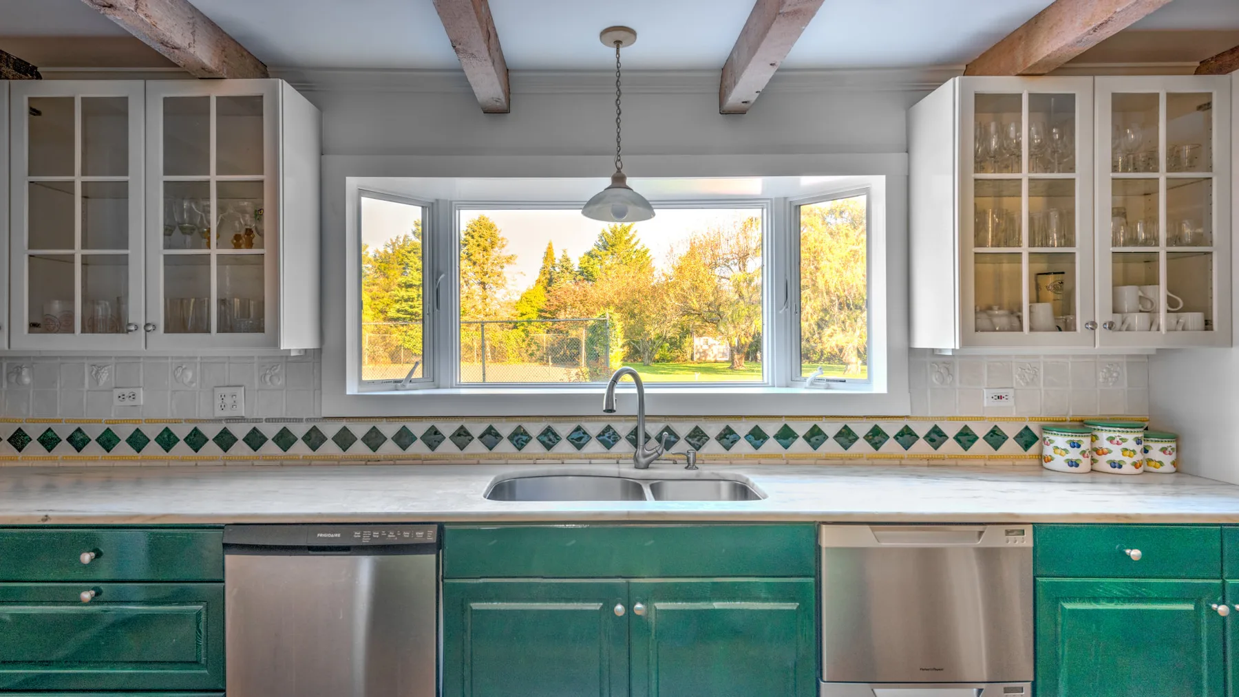 A kitchen with green cabinets, a central sink, and a wide window.