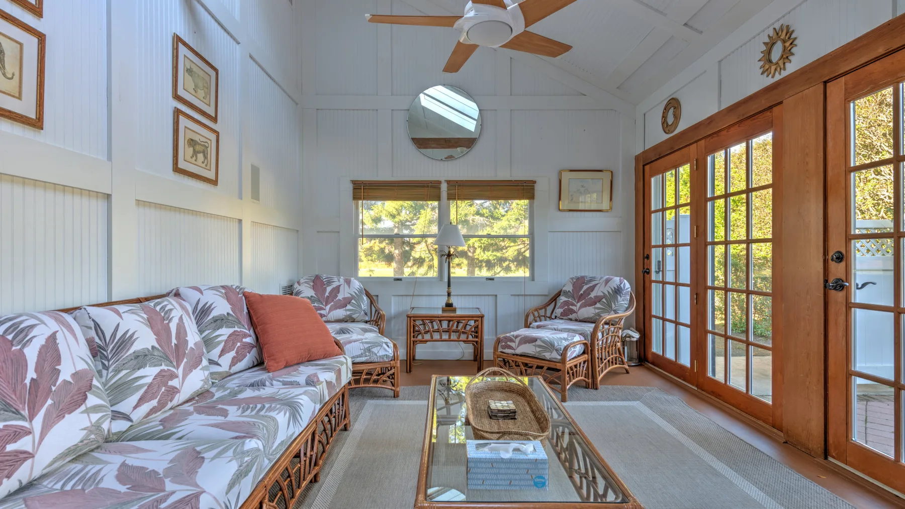A bright living room with patterned seating, a glass coffee table, and wooden doors.