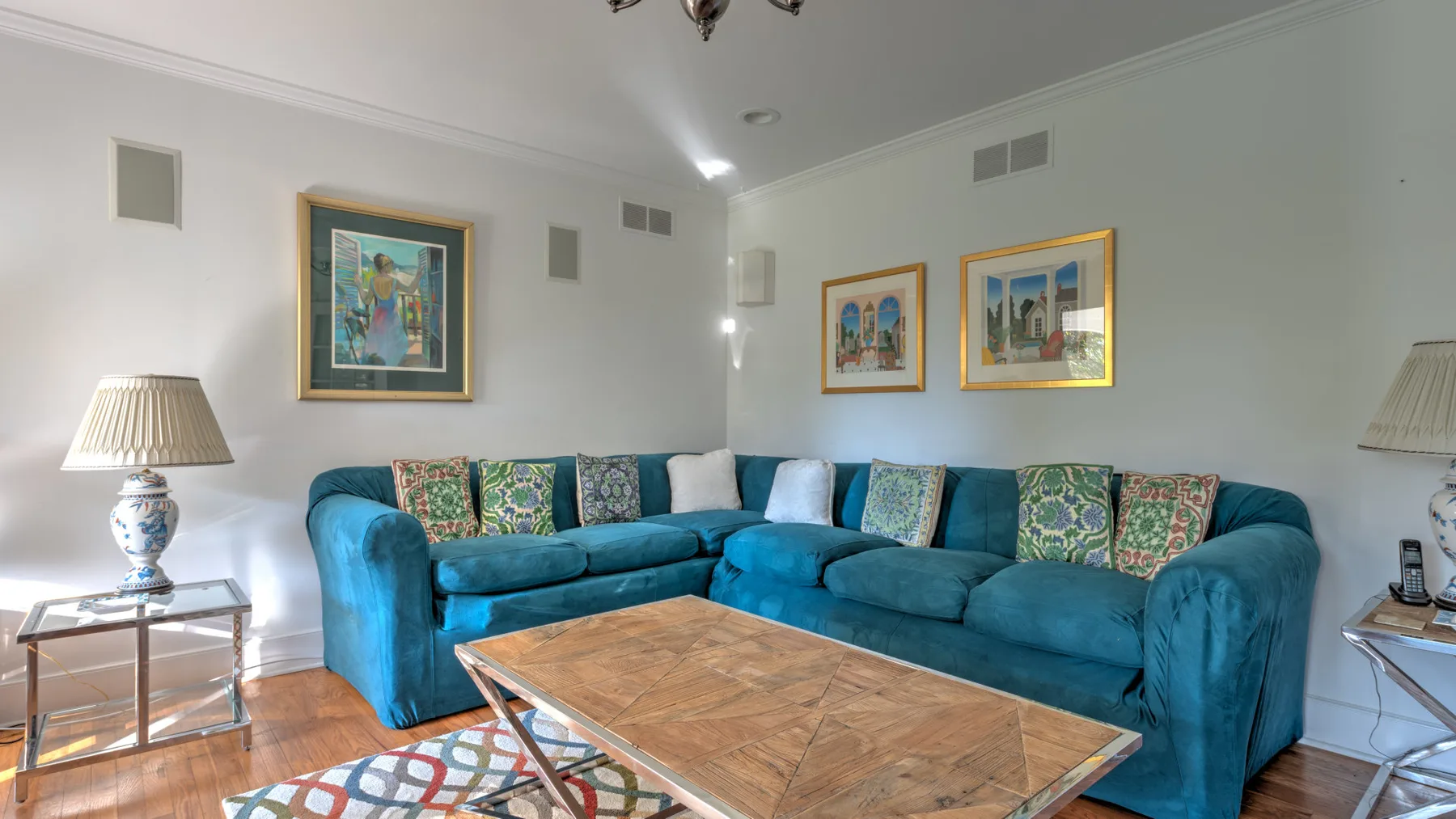 A living room with teal sectional seating, framed artwork, and a wooden coffee table.