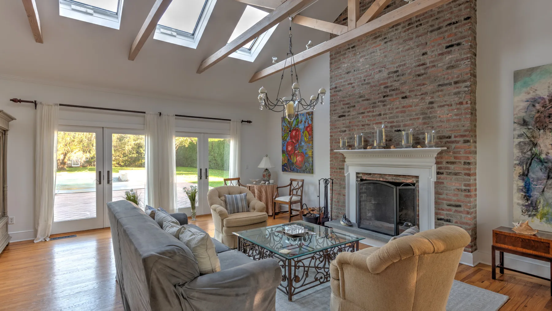 A bright living room with seating around a glass coffee table beside a brick fireplace.