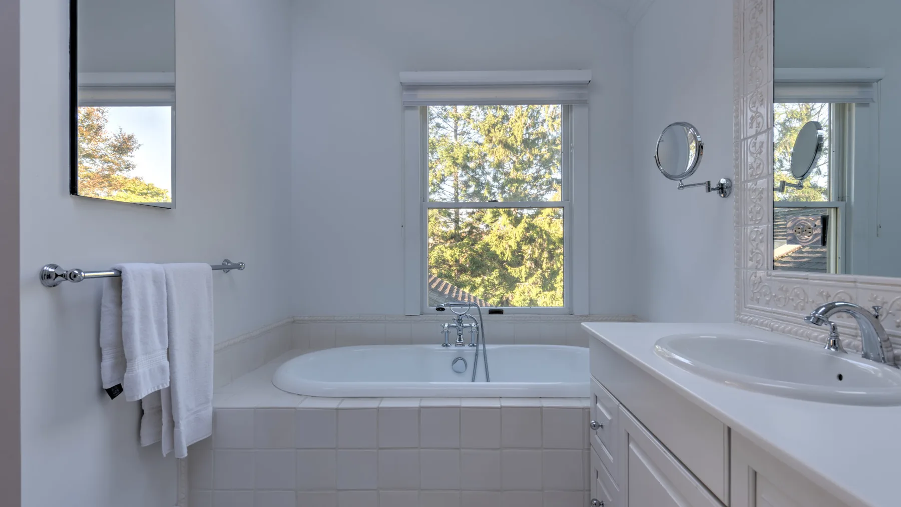 A bright bathroom with a bathtub beneath a window and a sink vanity.