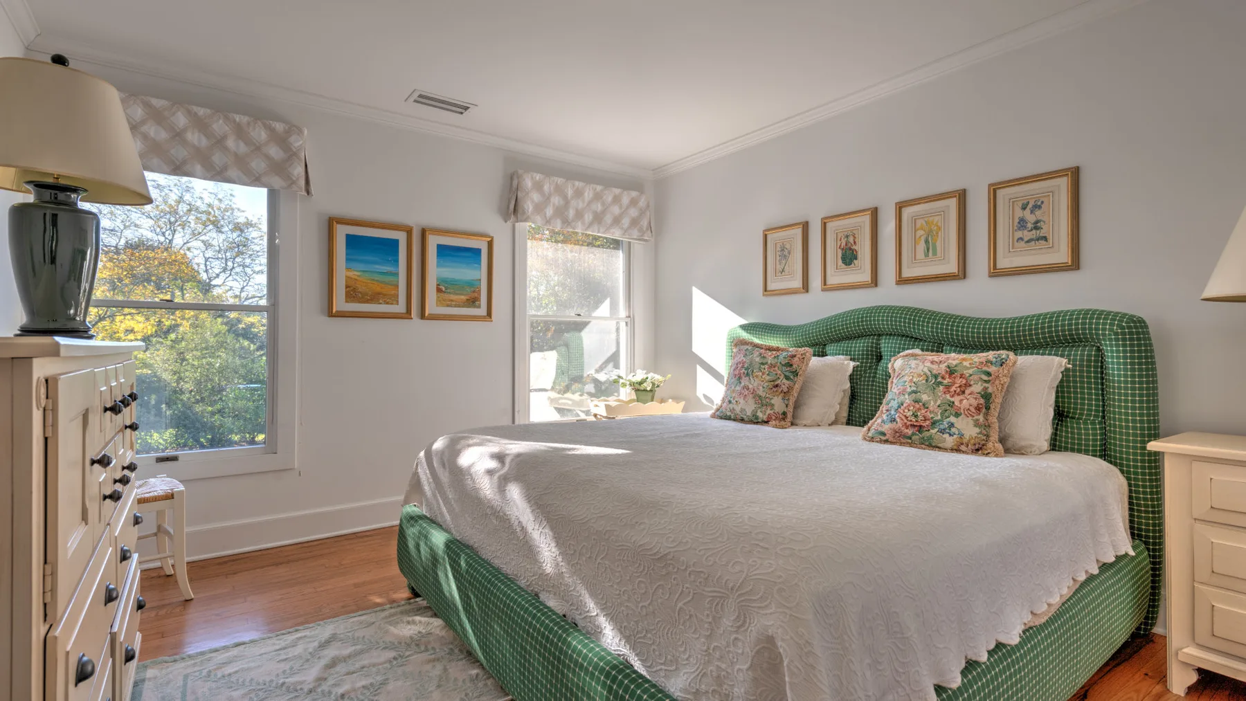 A bedroom with a green bed, framed artwork, and windows.
