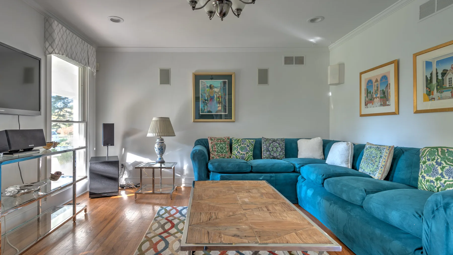 A living room with a teal sectional, wooden coffee table, and framed artwork.