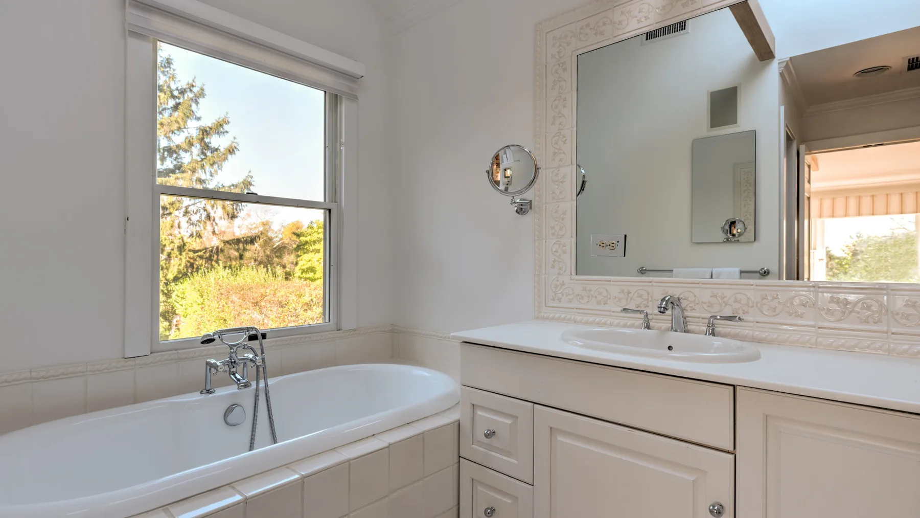 A bright bathroom with a bathtub, a large mirror, and a window.