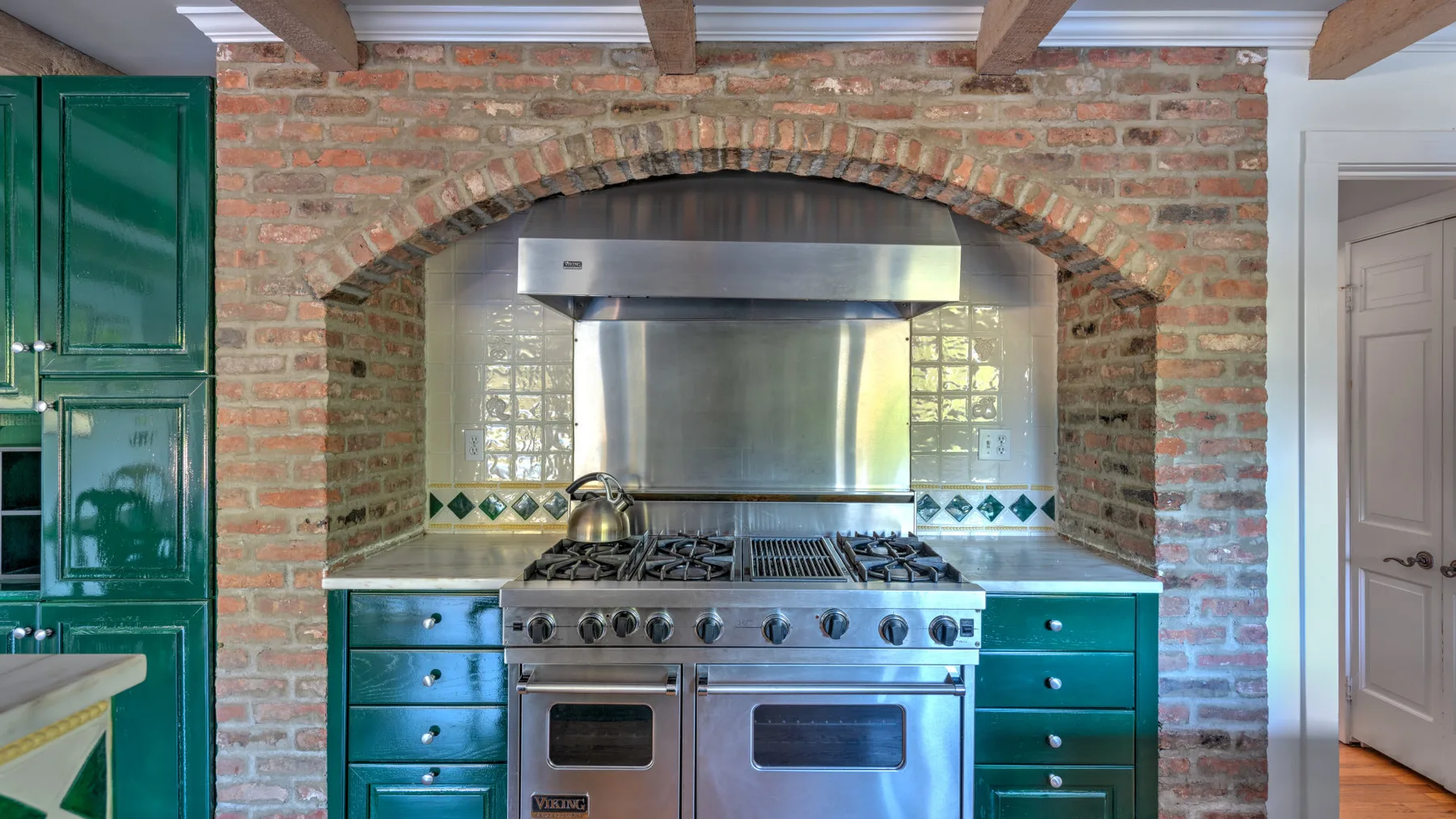 A kitchen with a stainless steel range beneath a brick arch.