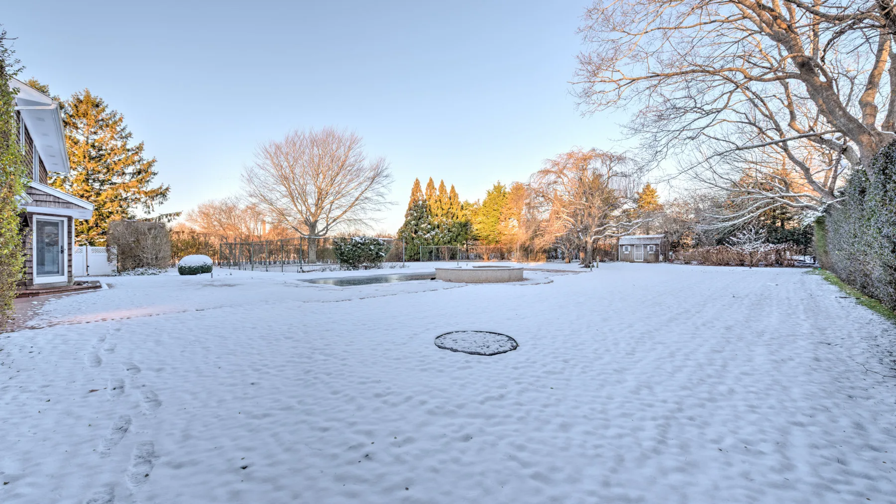 A snow-covered outdoor yard with bare trees and a small building at the edge.