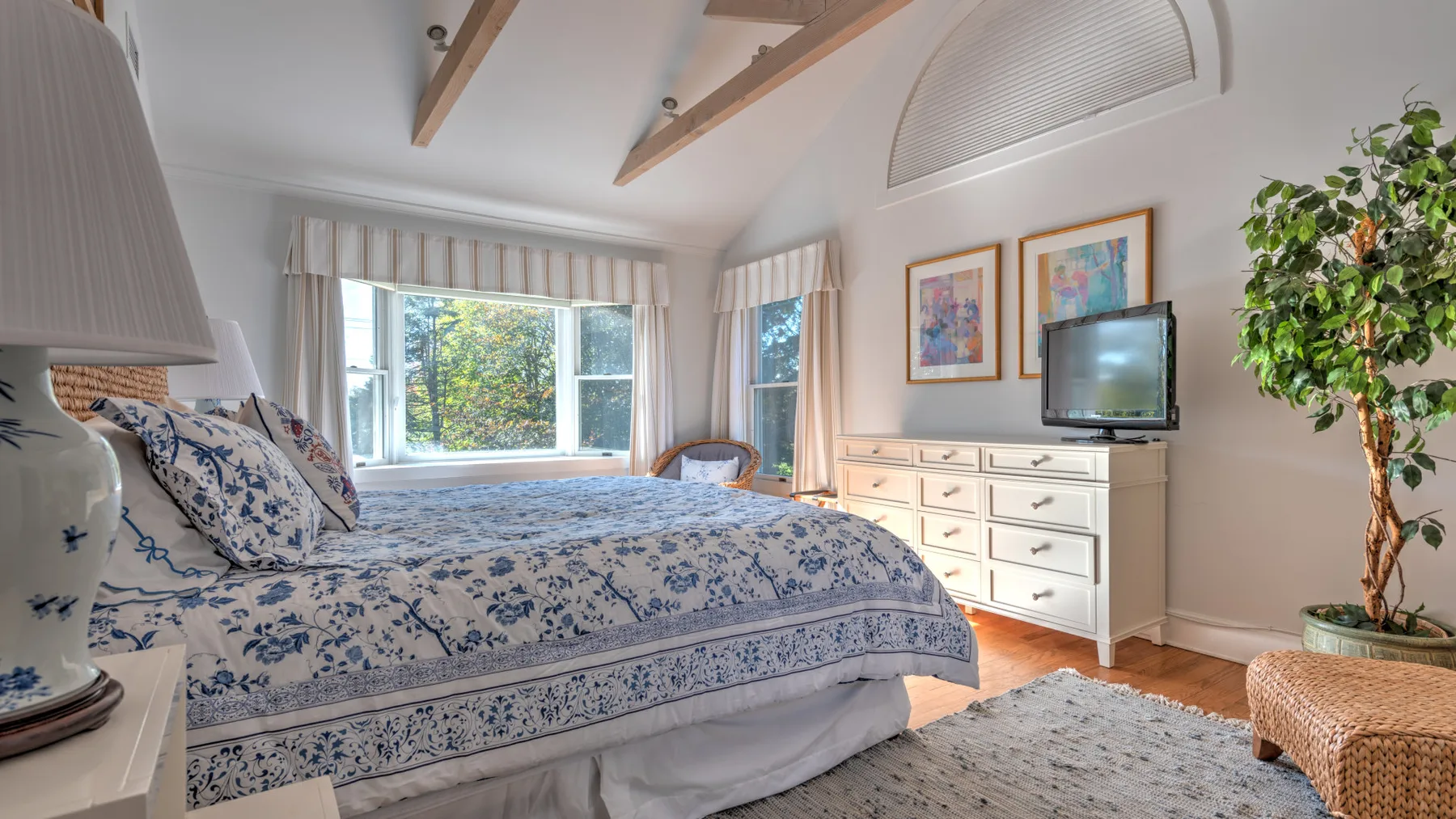 A bedroom with a bed, dresser, and large windows.