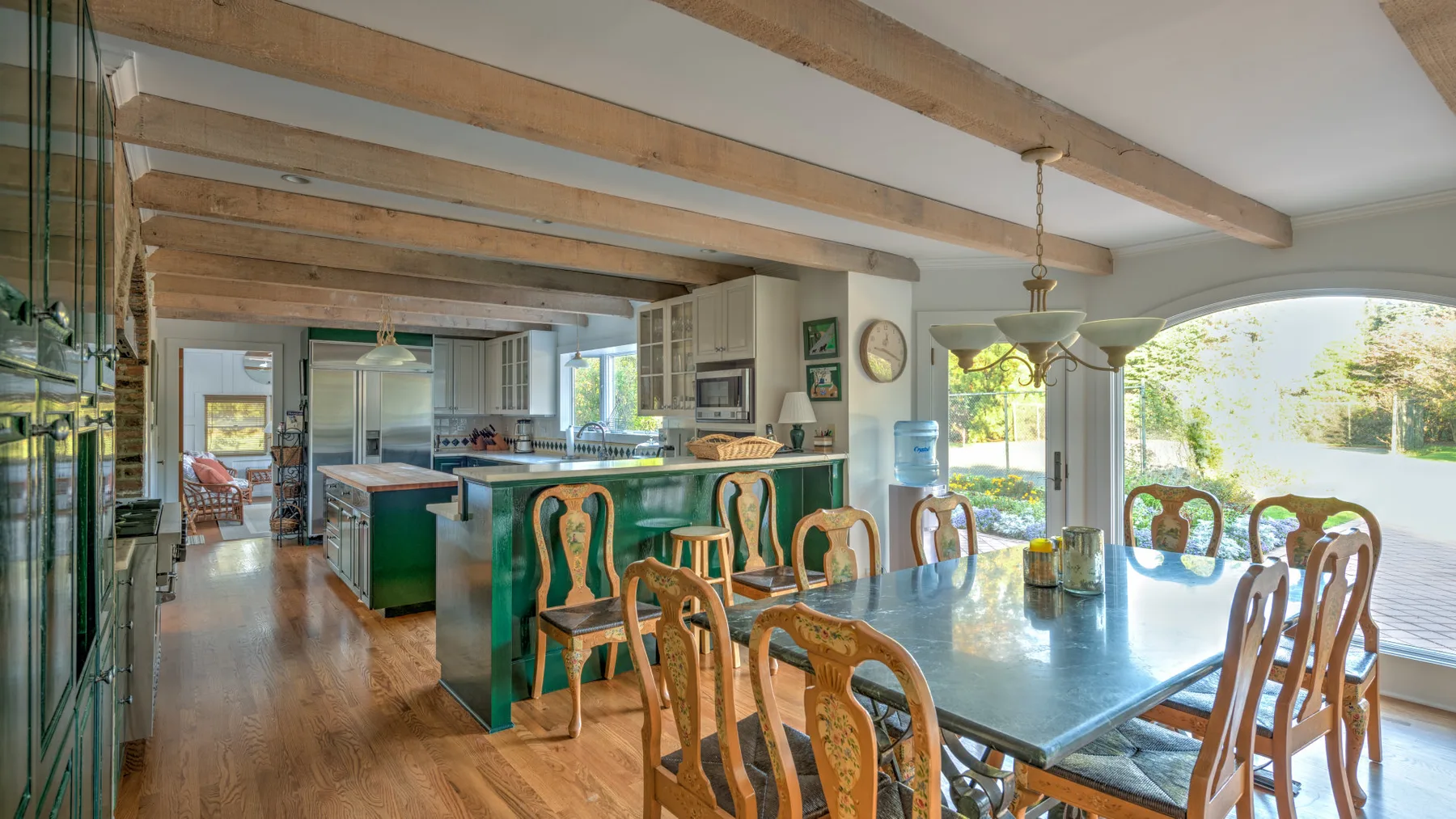 An open kitchen and dining area with a long table beneath exposed wooden beams.
