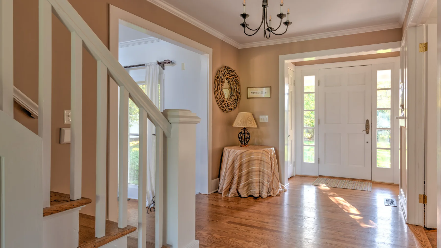 A bright home entryway with a staircase, a small table, and a white front door.
