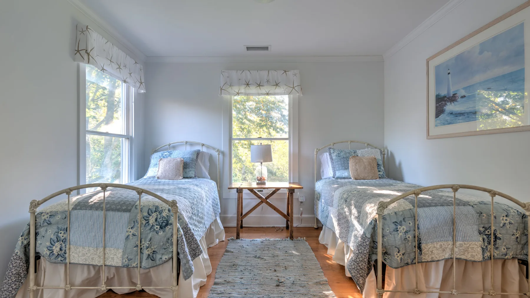 A bright bedroom with two beds and a small table between them.