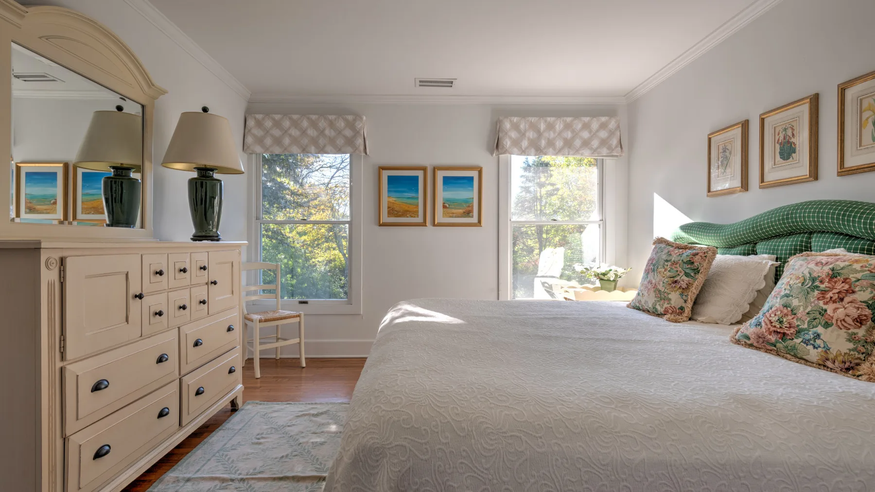 A bright bedroom with a large bed, windows, and a dresser.