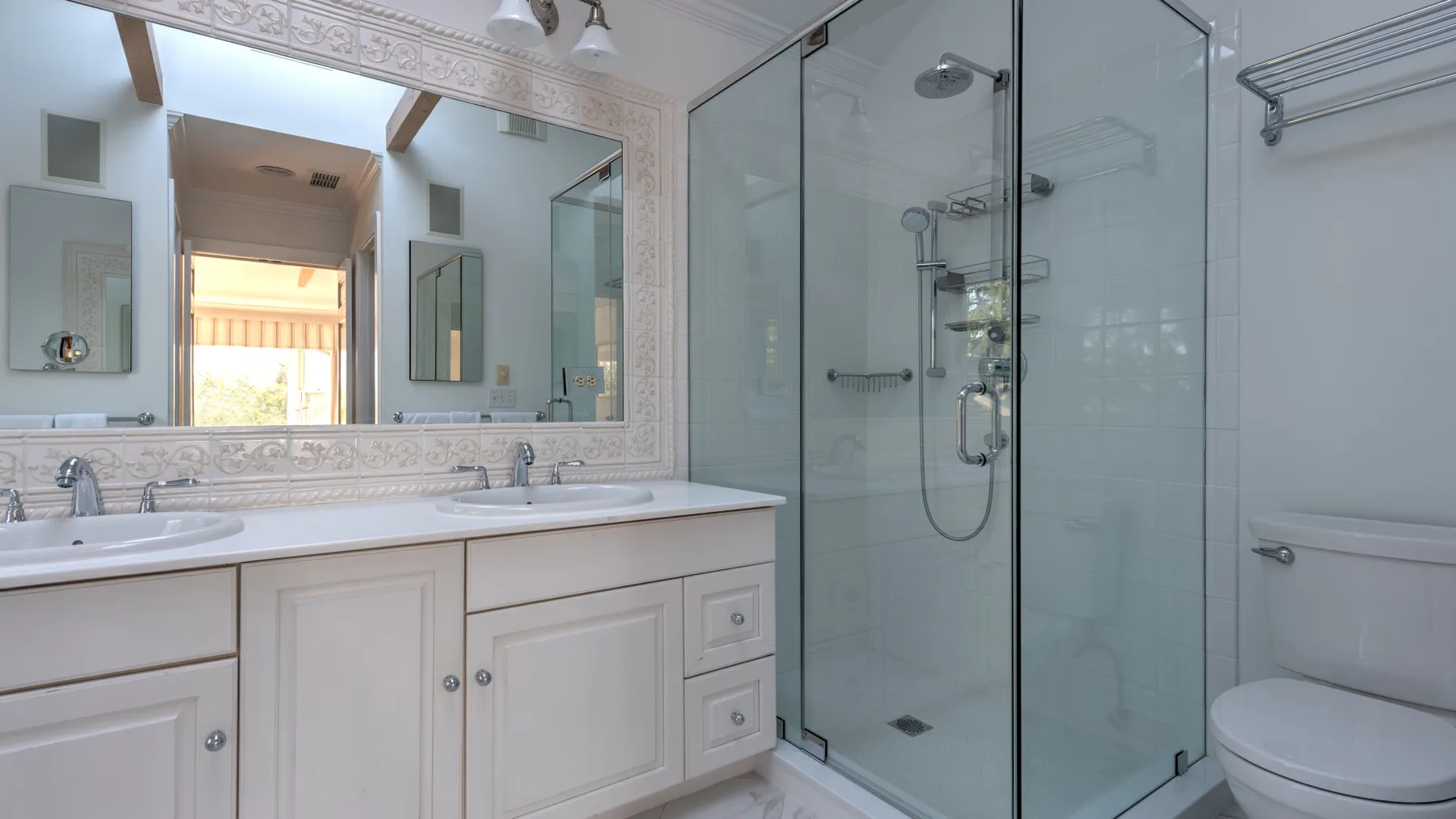 A bathroom with a double vanity, large mirror, and glass shower.