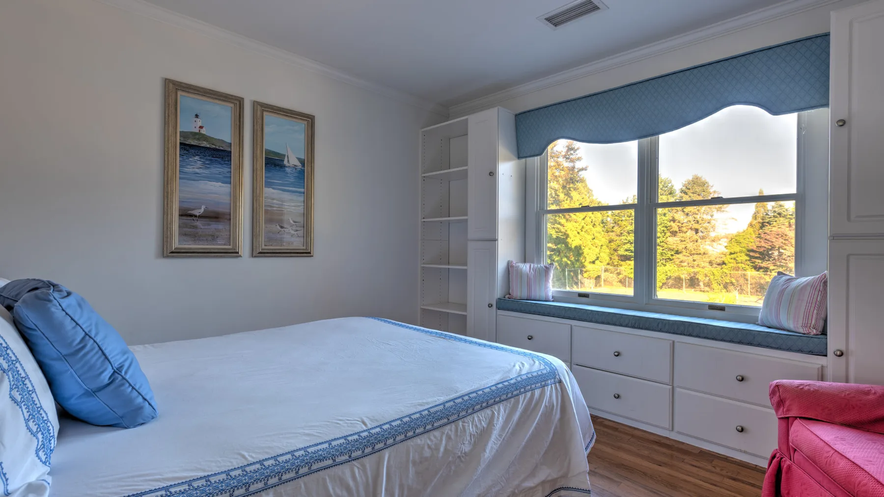 A bedroom with a bed beside a wide window and built-in drawers.