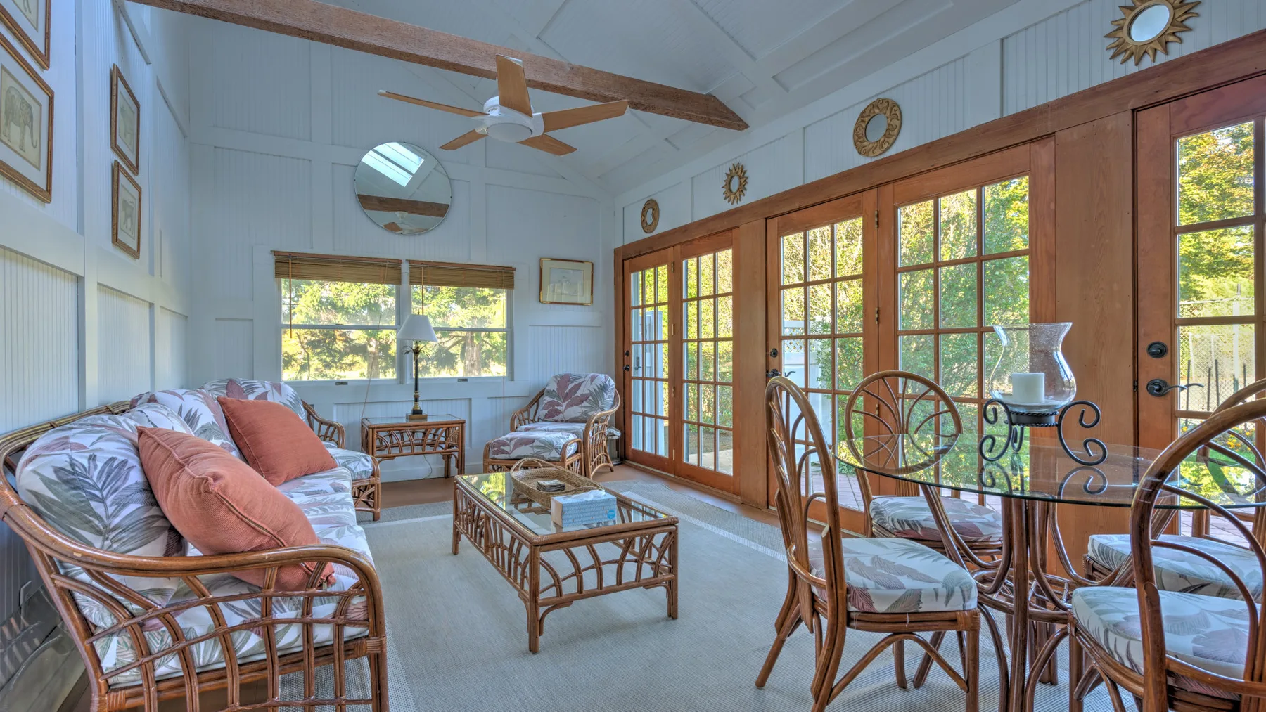 A bright sunroom has wicker seating, a glass-topped table, and large windows.