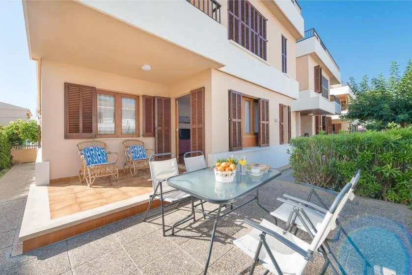 Un patio soleado con asientos al aire libre y una mesa de vidrio junto a un edificio residencial.