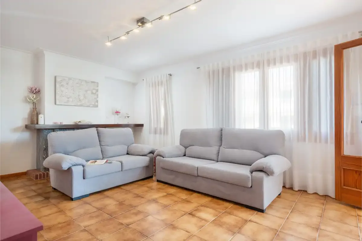 Una sala de estar luminosa con sofás, una consola de madera y cortinas traslúcidas.