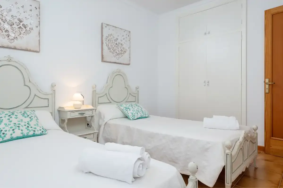 Un dormitorio con camas, almohadas estampadas en turquesa y cuadros en la pared.