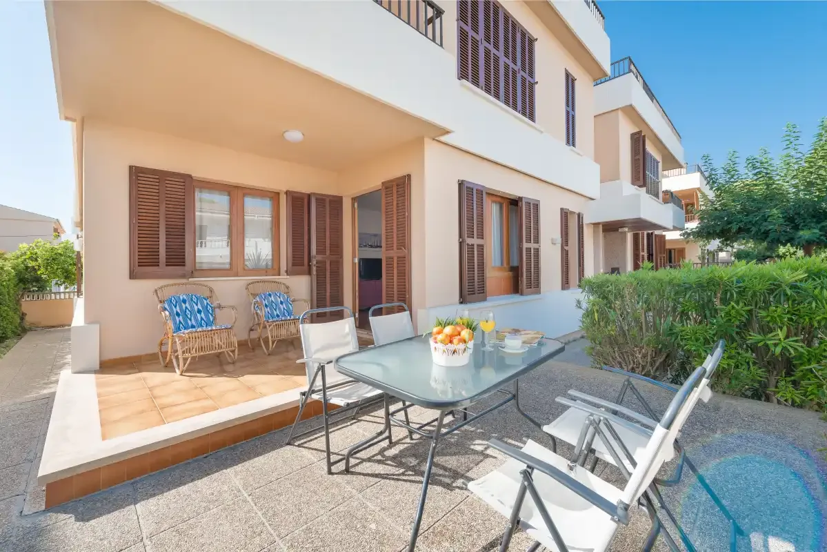 Un comedor en el patio con una mesa de cristal y asientos junto a una casa.