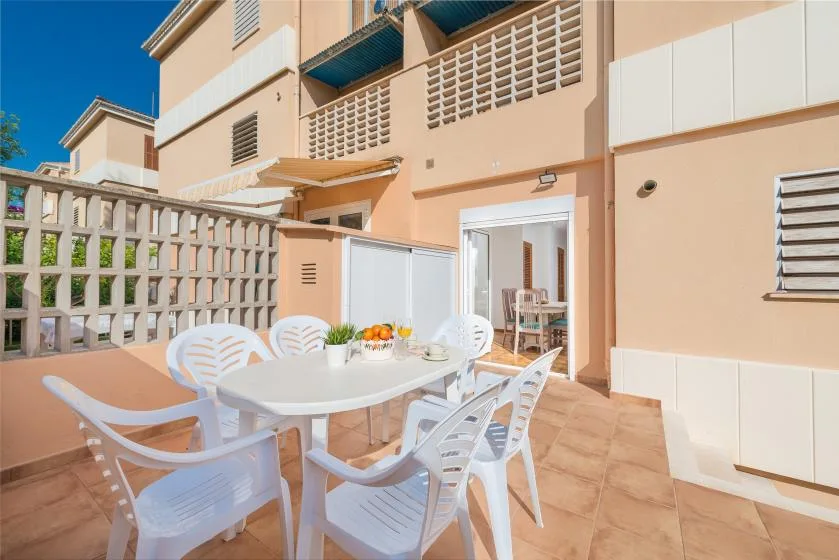 Un patio embaldosado tiene asientos blancos alrededor de una mesa junto a una puerta abierta.