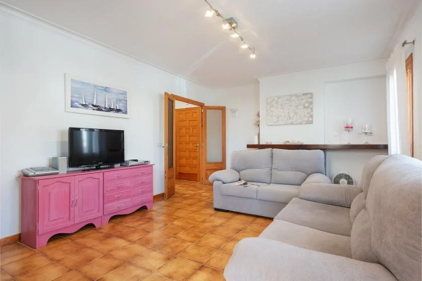 Sala de estar con un televisor sobre un mueble rosa y asientos de tono claro.