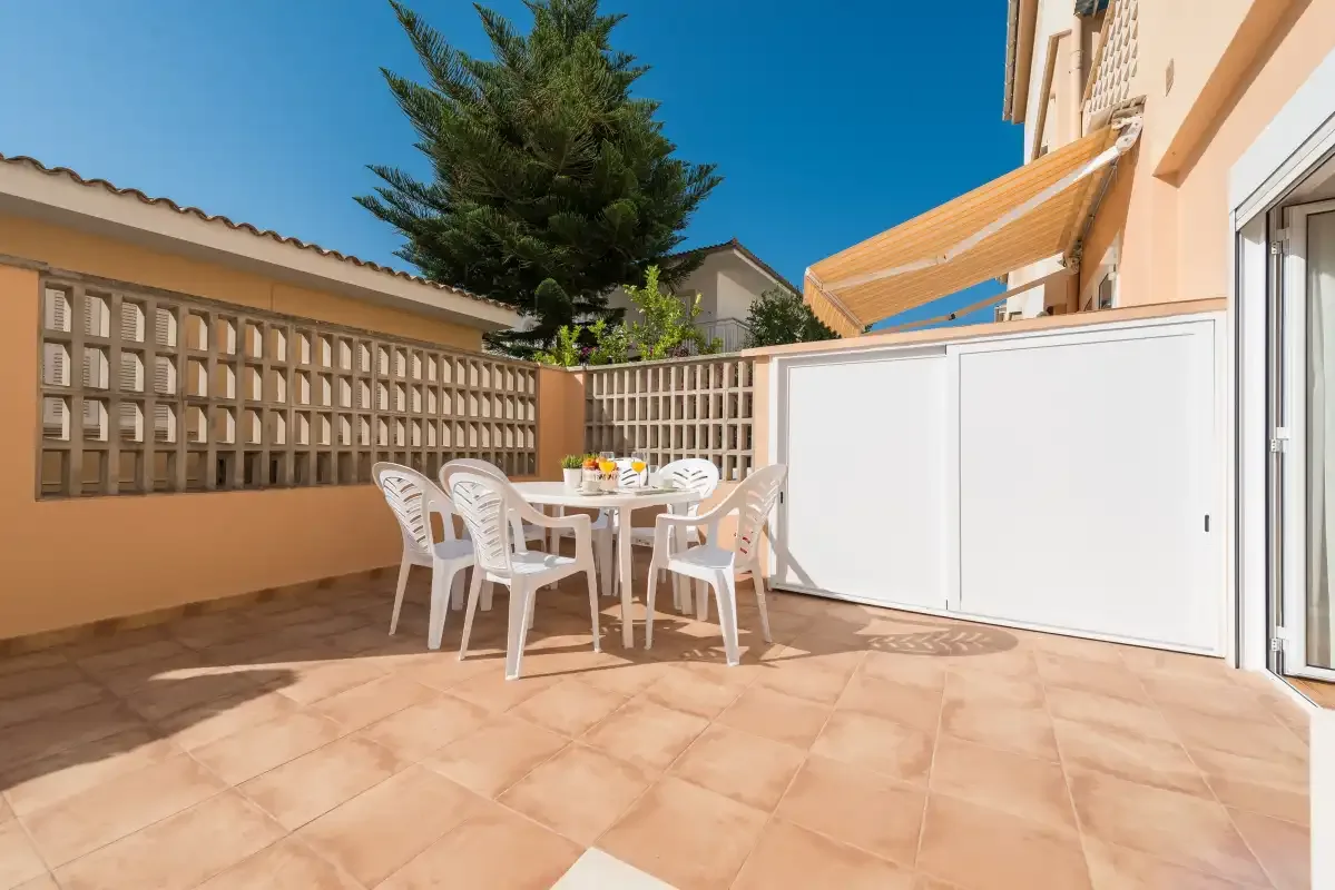 Un patio soleado con una mesa de comedor y asientos blancos.