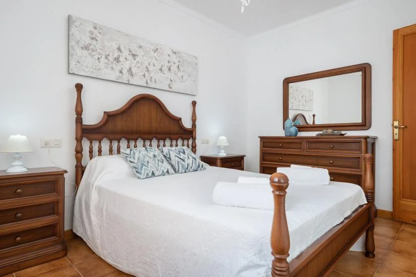 Un dormitorio con una cama de madera, ropa de cama blanca y una cómoda bajo un espejo.