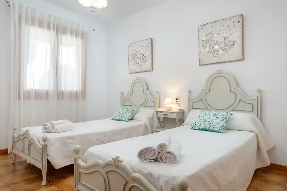 Un dormitorio luminoso con dos camas, cojines estampados y cuadros florales.