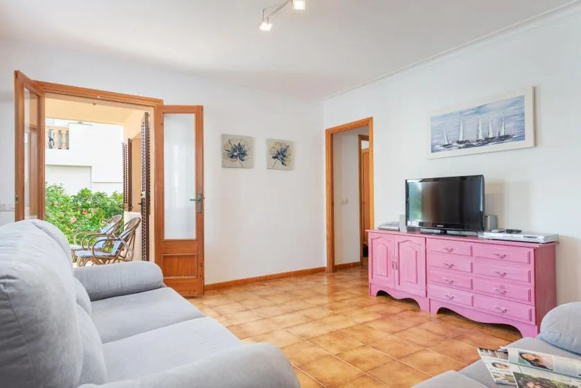 Una sala luminosa con asientos, un televisor y una puerta abierta hacia un balcón.