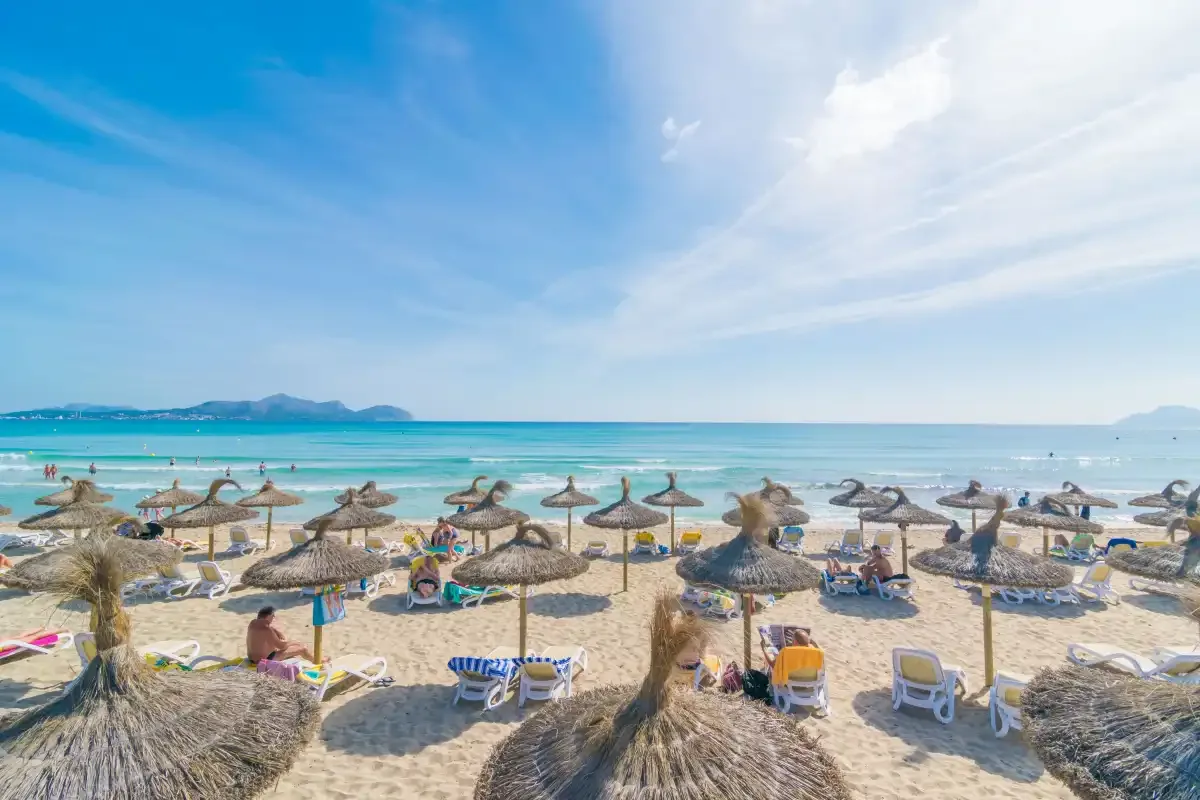 Una playa de arena con sombrillas de paja junto al agua turquesa.