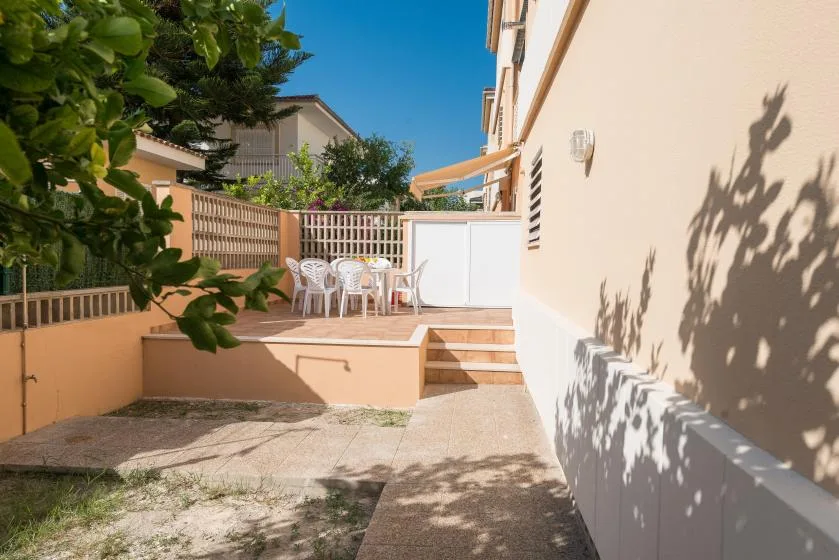 Un patio soleado con asientos, escalones y una puerta blanca junto al edificio.