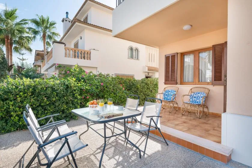 Un patio soleado con asientos al aire libre y un seto junto a la casa.