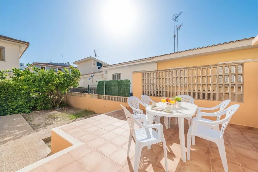 Un patio soleado con una mesa blanca y sillas junto a una pared de celosía.