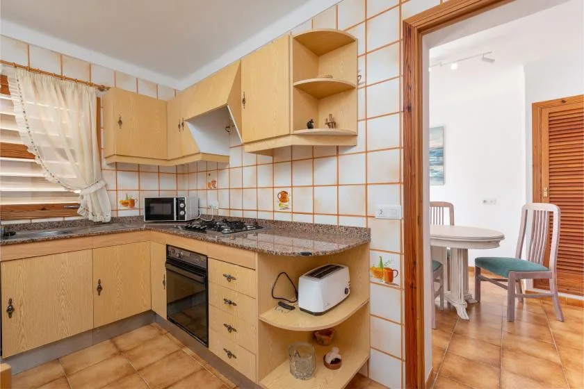 Una cocina alicatada con armarios de madera y un comedor visible a través de la puerta.