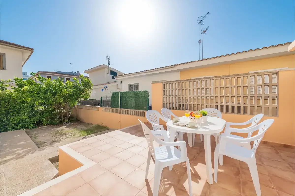 Un patio exterior soleado tiene sillas blancas de plástico alrededor de una mesa.