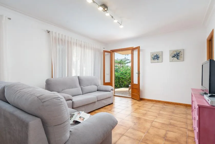 Una luminosa sala de estar con asientos grises y una puerta abierta hacia la vegetación.