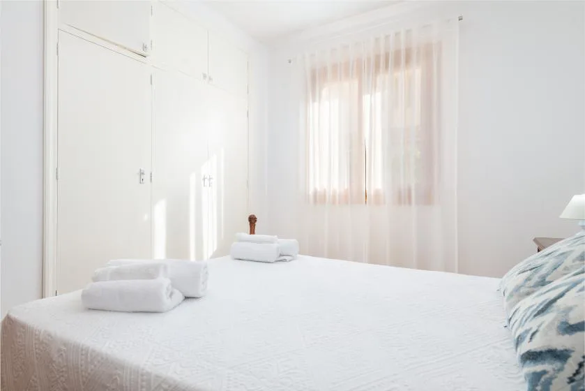 Un dormitorio luminoso con una cama bien arreglada y toallas dobladas.