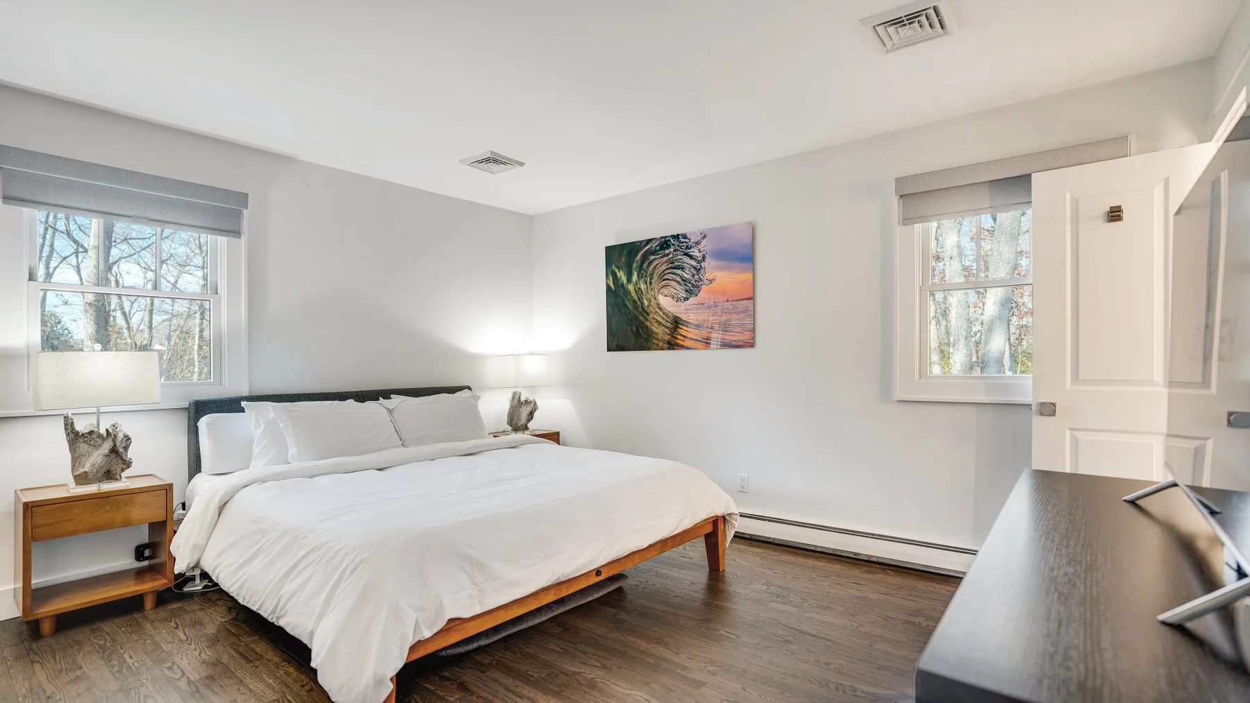 A bright bedroom with a neatly made bed and windows on two walls.