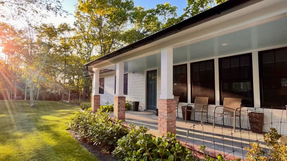 A covered outdoor seating area overlooks a grassy yard and leafy garden.