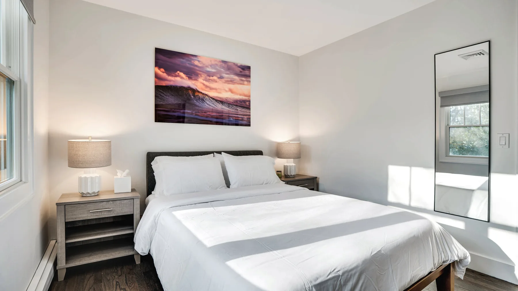 A bright bedroom with a neatly made bed and a framed landscape above it.