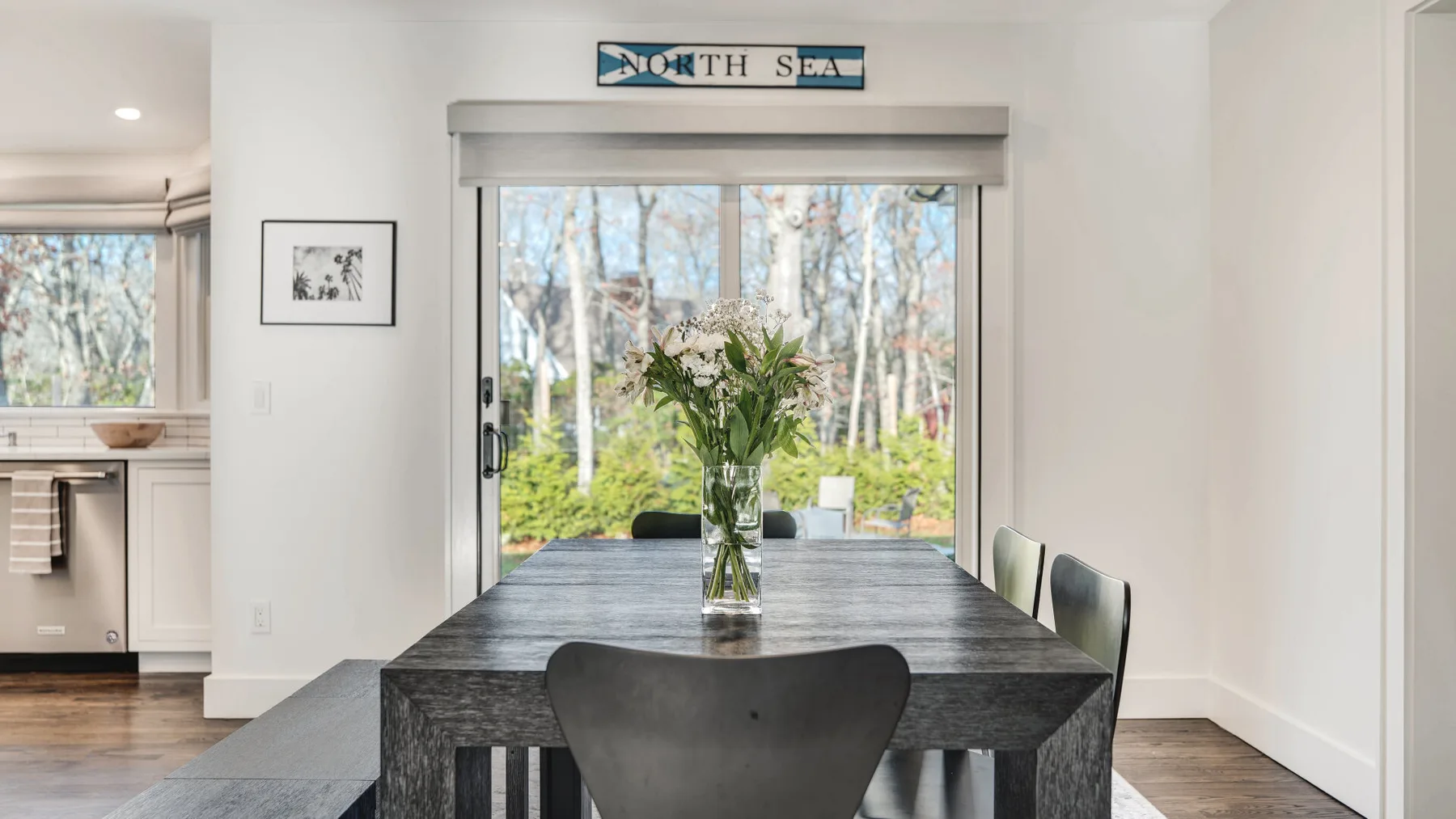 A dining area with a dark table and flowers beside a large window.