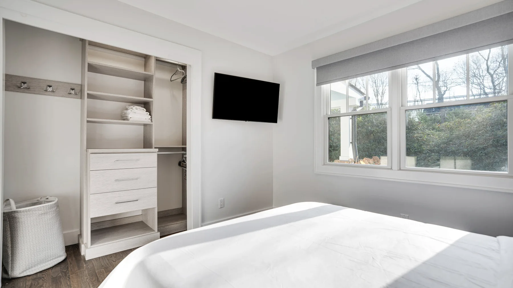 A bright bedroom with a bed, open closet, and wall-mounted television.