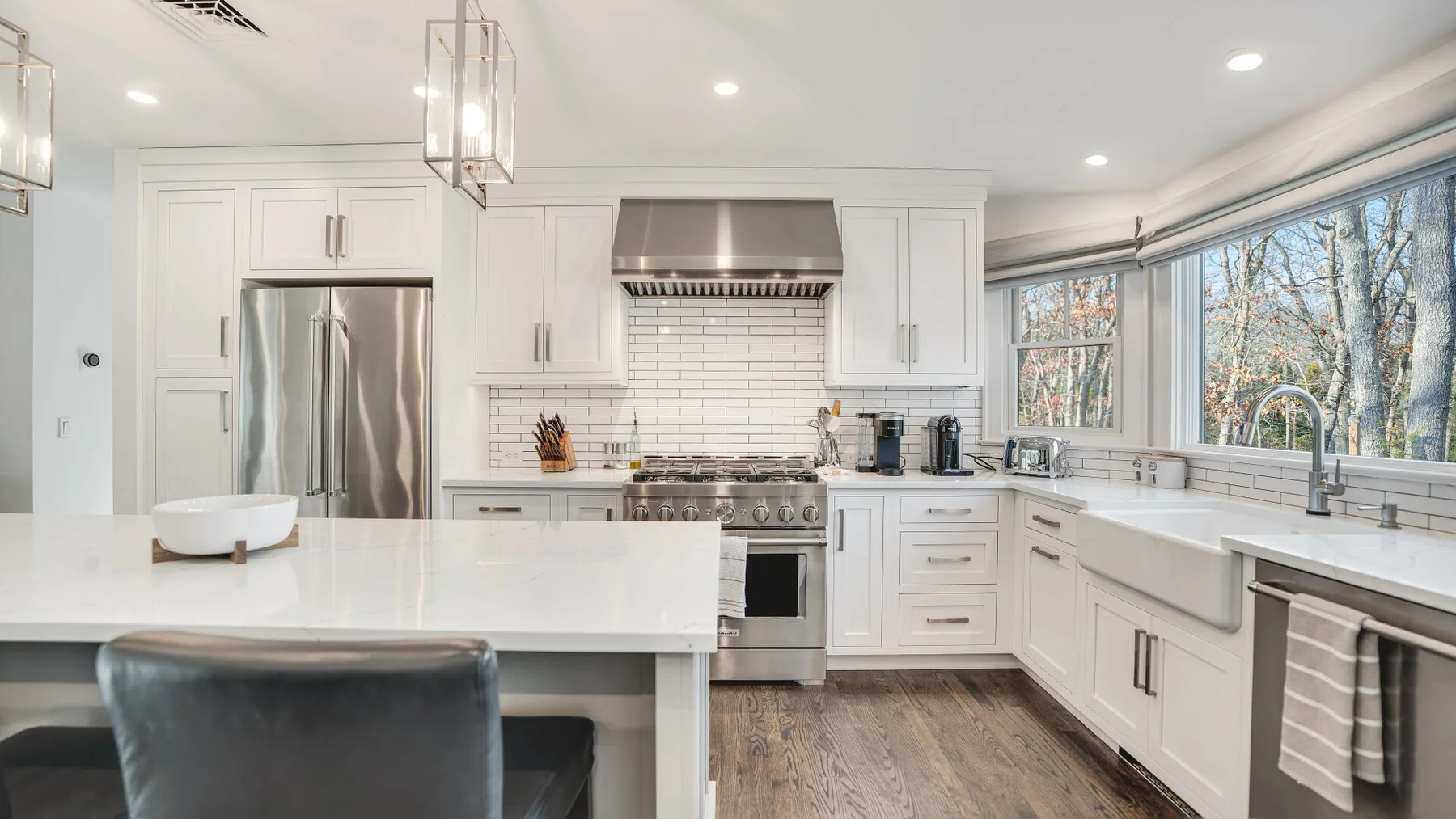 A bright white kitchen with a large island, stainless steel appliances, and broad windows.