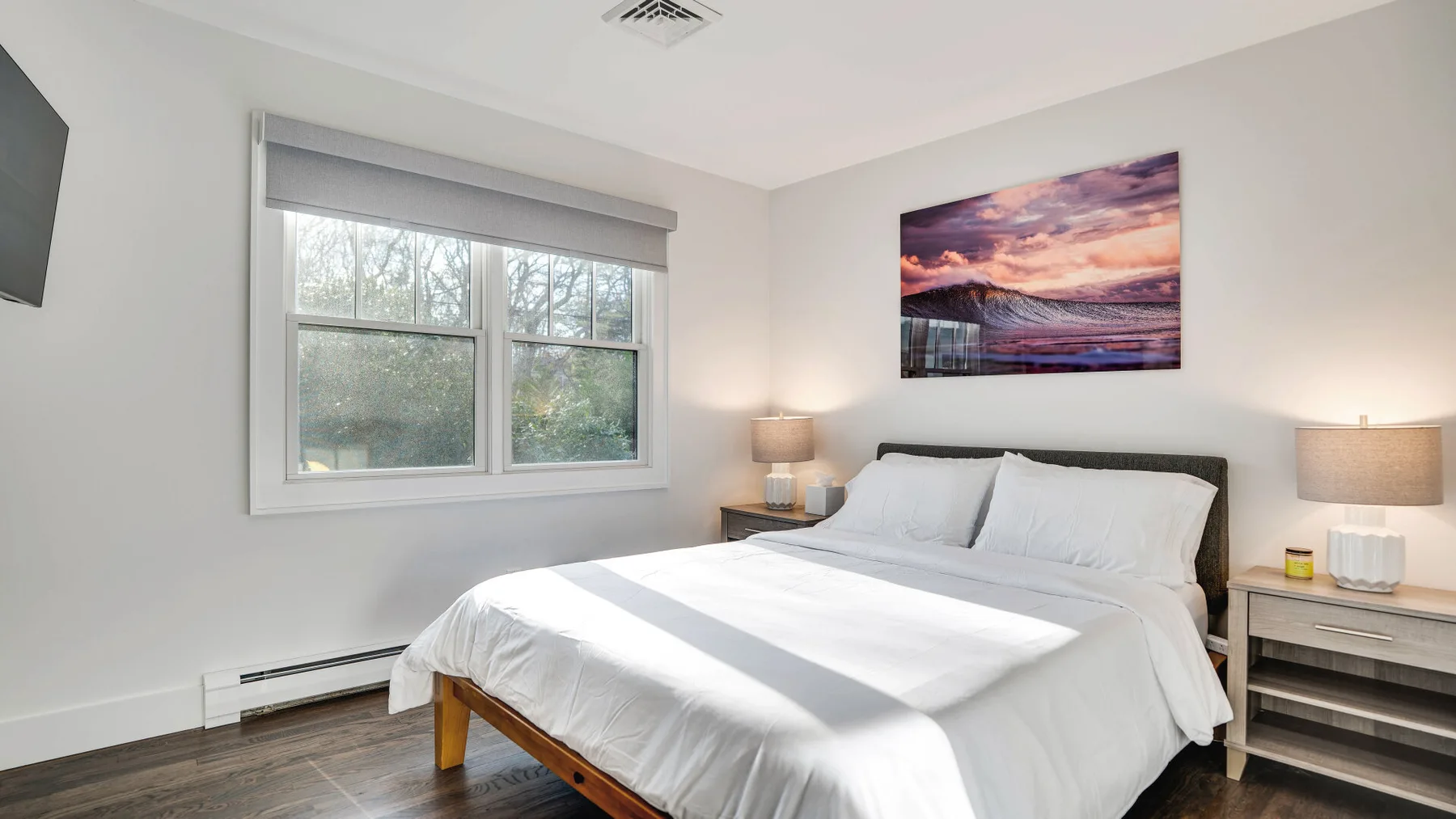 A bright bedroom with a neatly made bed and a large window.