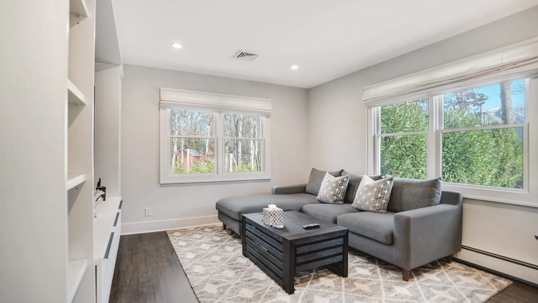 A bright living room with gray seating, a coffee table, and large windows.