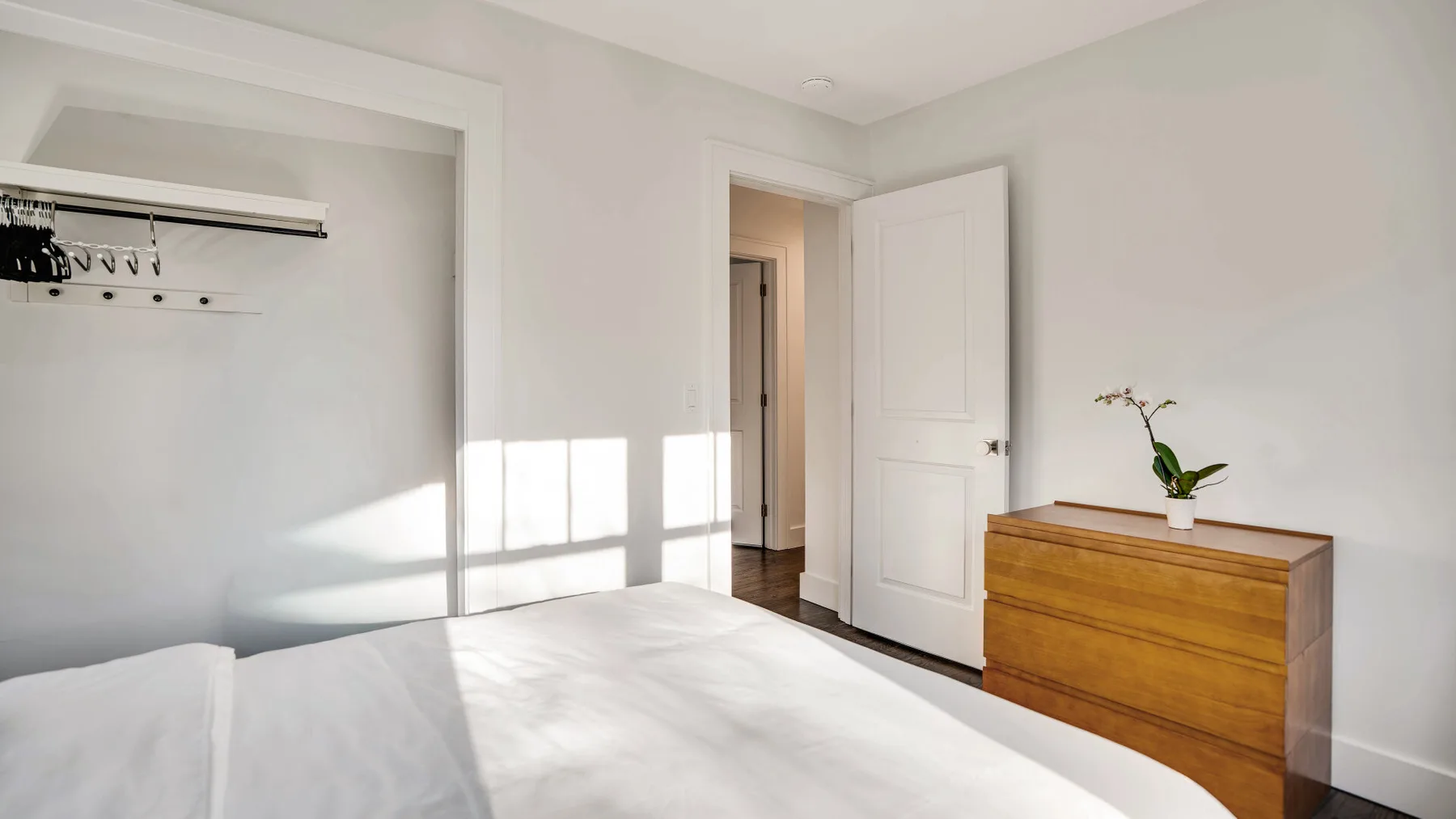 A bright bedroom with a bed, an open doorway, and a wooden dresser.