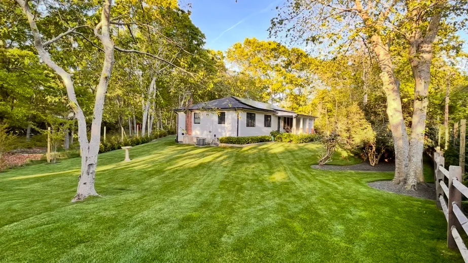 A single-story house sits beyond a broad green lawn bordered by trees.